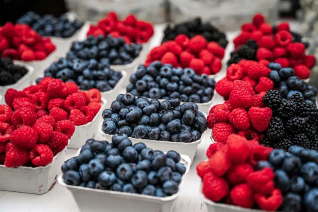 Fresh strawberries, blueberries, and raspberries in clear containers on a laboratory bench with testing equipment visible in the background